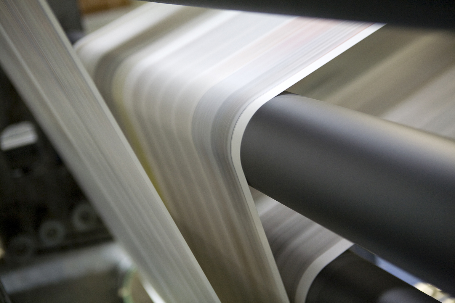 Paper travelling through print machine rollers at speed.